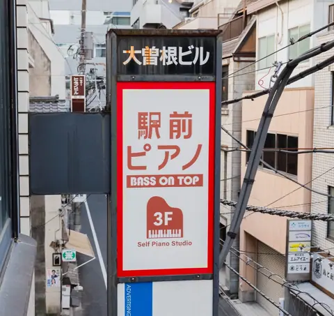 駅前ピアノ ベースオントップ神田店：ビルの駅前ピアノの看板