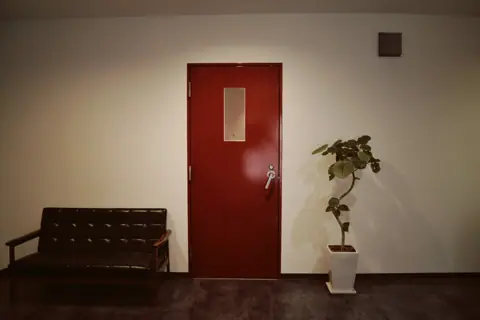 IFF STUDIO:赤い扉とソファのある通路
